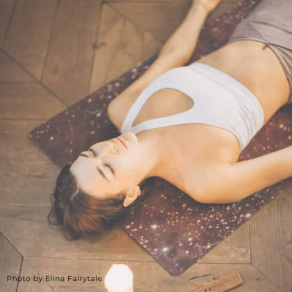 woman laying on floor in savasana with candles for online yoga nidra classes
